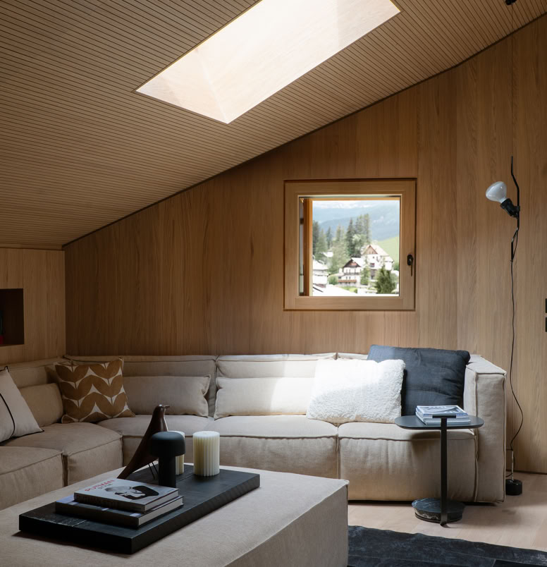 Spacious living room in luxury penthouse Cortina d’Ampezzo with designer sofa, armchairs, natural light, and wooden finishes.