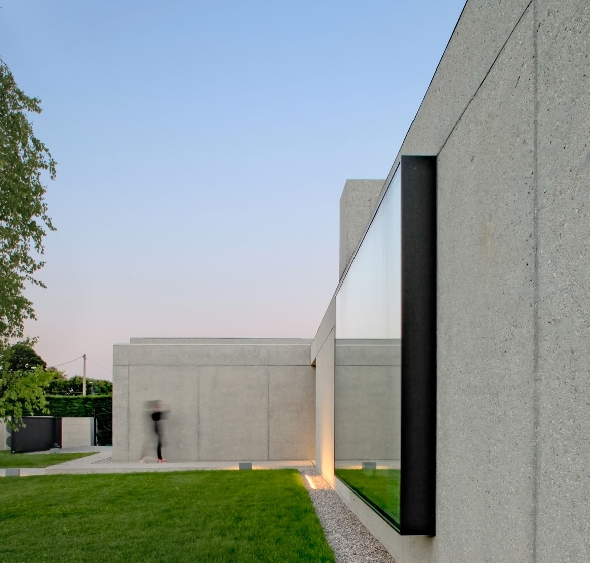 Villa unifamiliare su un unico piano progettata da MIDE architetti, con volumi essenziali in calcestruzzo sabbiato e ampie vetrate rivolte al giardino.