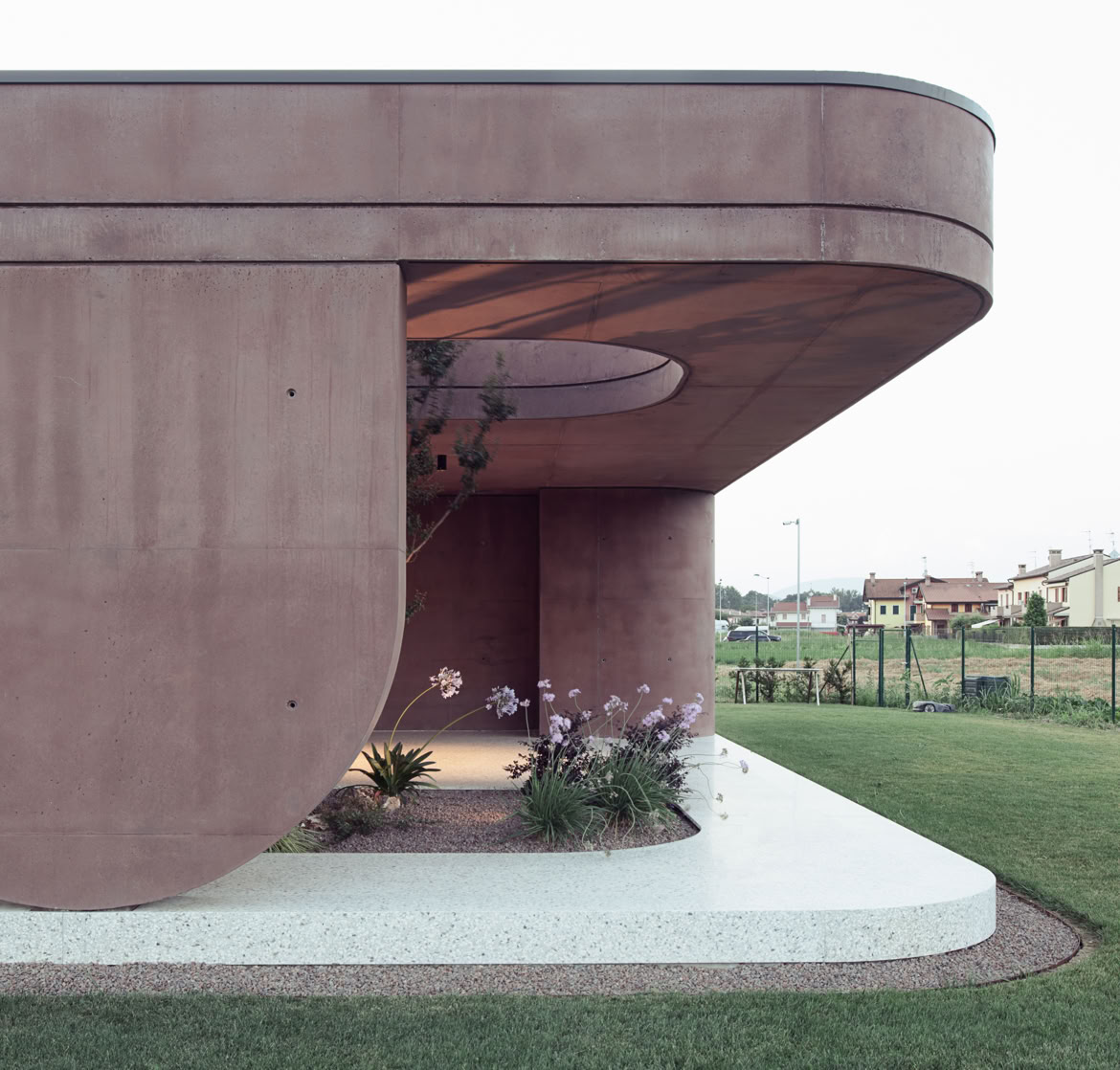 Le curve morbide della villa firmata da MIDE architetti accolgono al loro interno arbusti e alberi che dialogano con la matericità del calcestruzzo.
