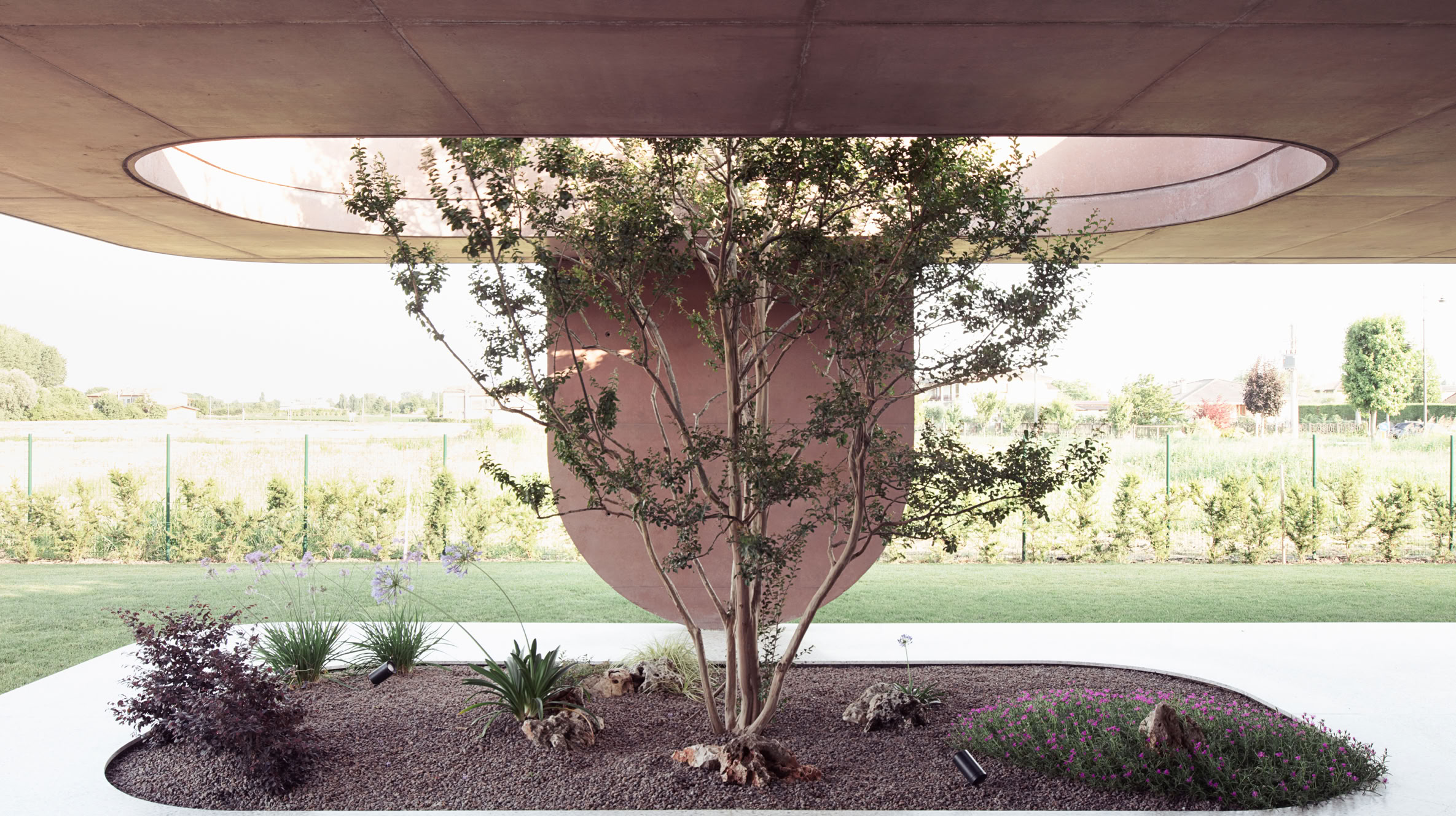 Vista dell'ampio portico con pilastri materici e aperture con vegetazione inserita. 