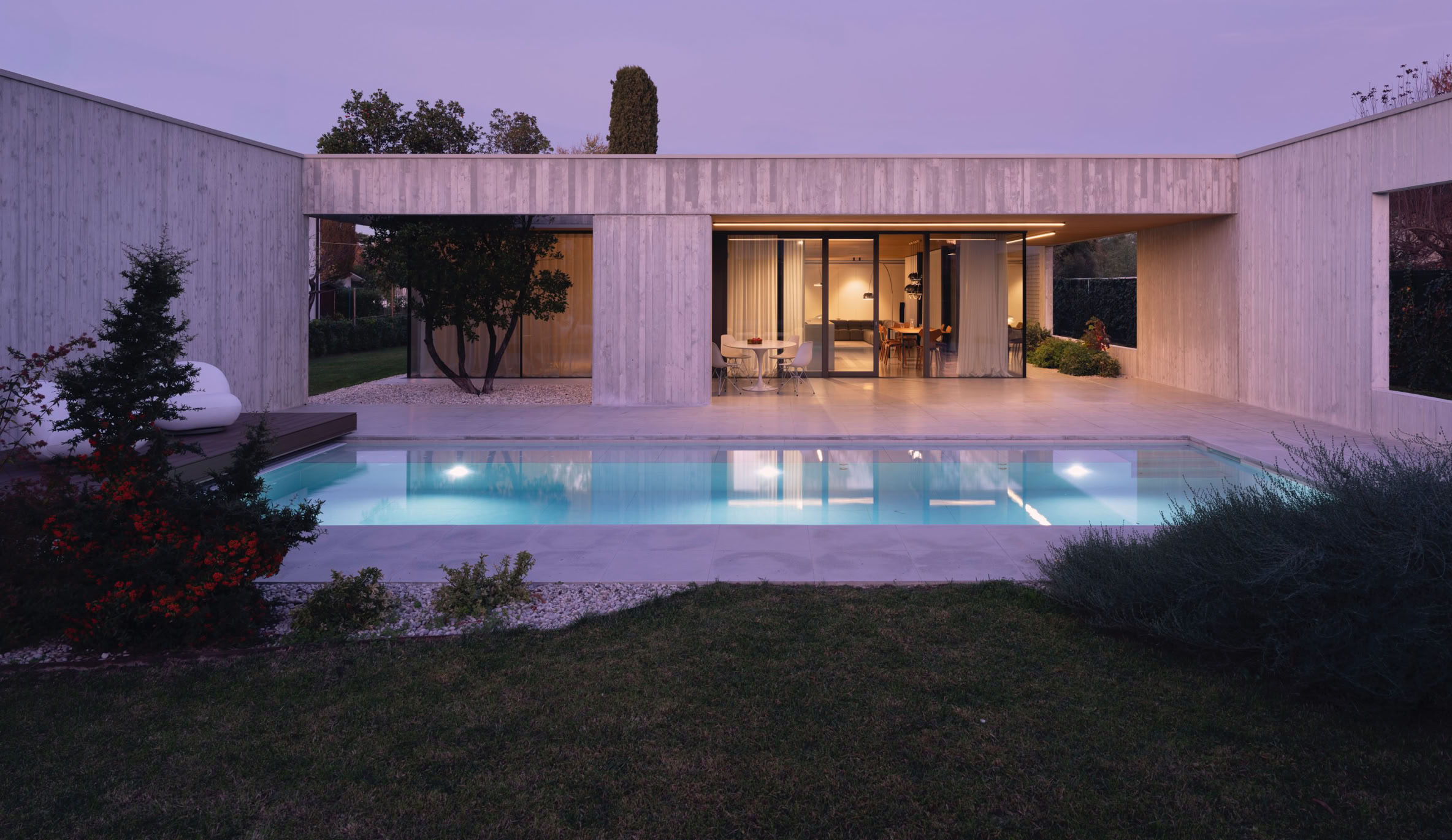 Evening view of the outdoor pool at the Piave villa designed by MIDE architetti, highlighting the integration of water, architecture, and natural surroundings.
