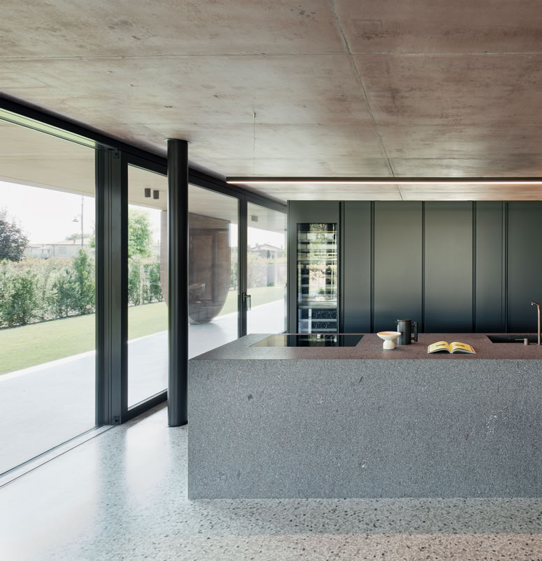 Cucina open space della villa progettata da MIDE architetti, dove il calcestruzzo colorato dialoga con la vegetazione, creando un’atmosfera sospesa tra interno ed esterno.