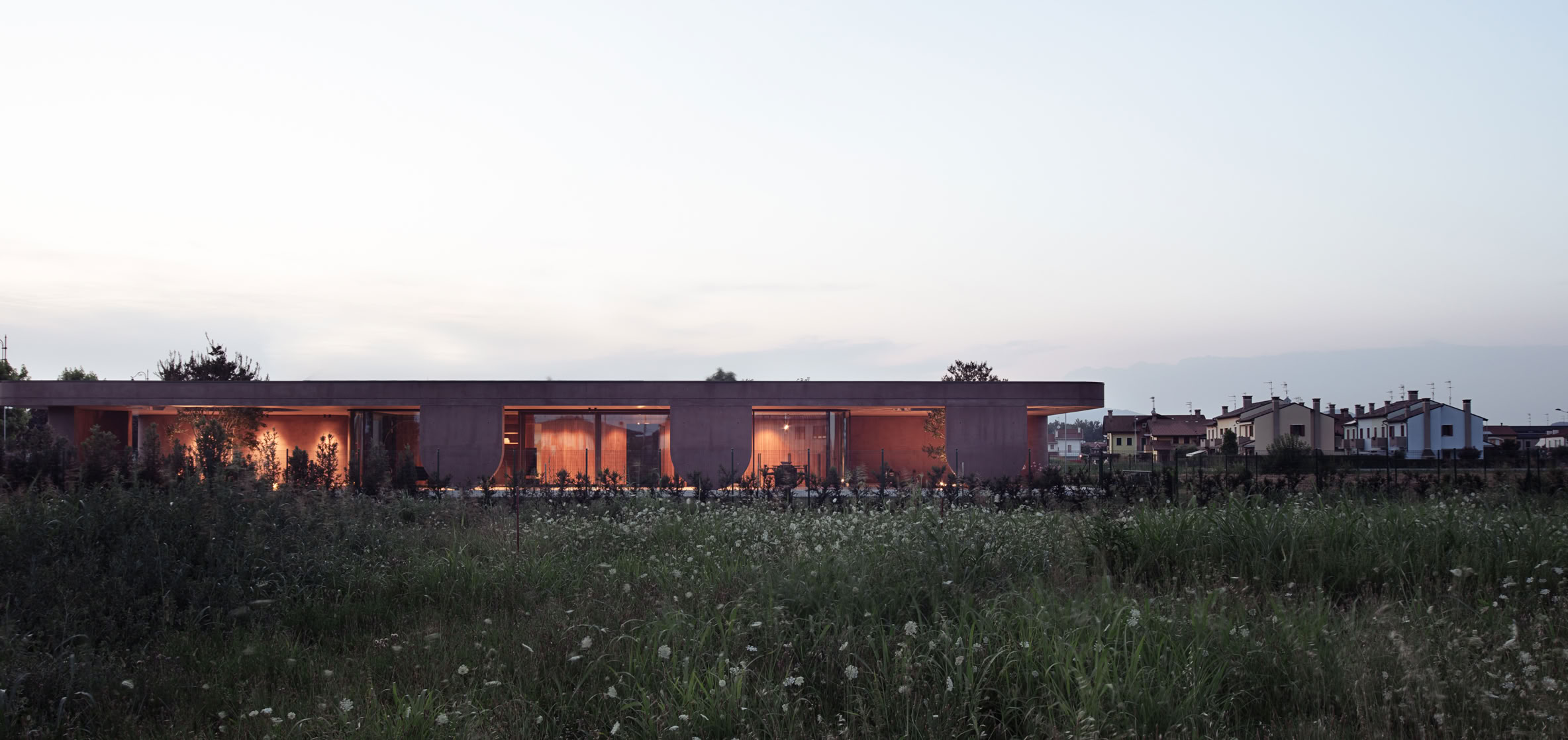 Facciata scenica della villa progettata da MIDE architetti con volumi e aperture che permettono di incorniciare il verde circostante.